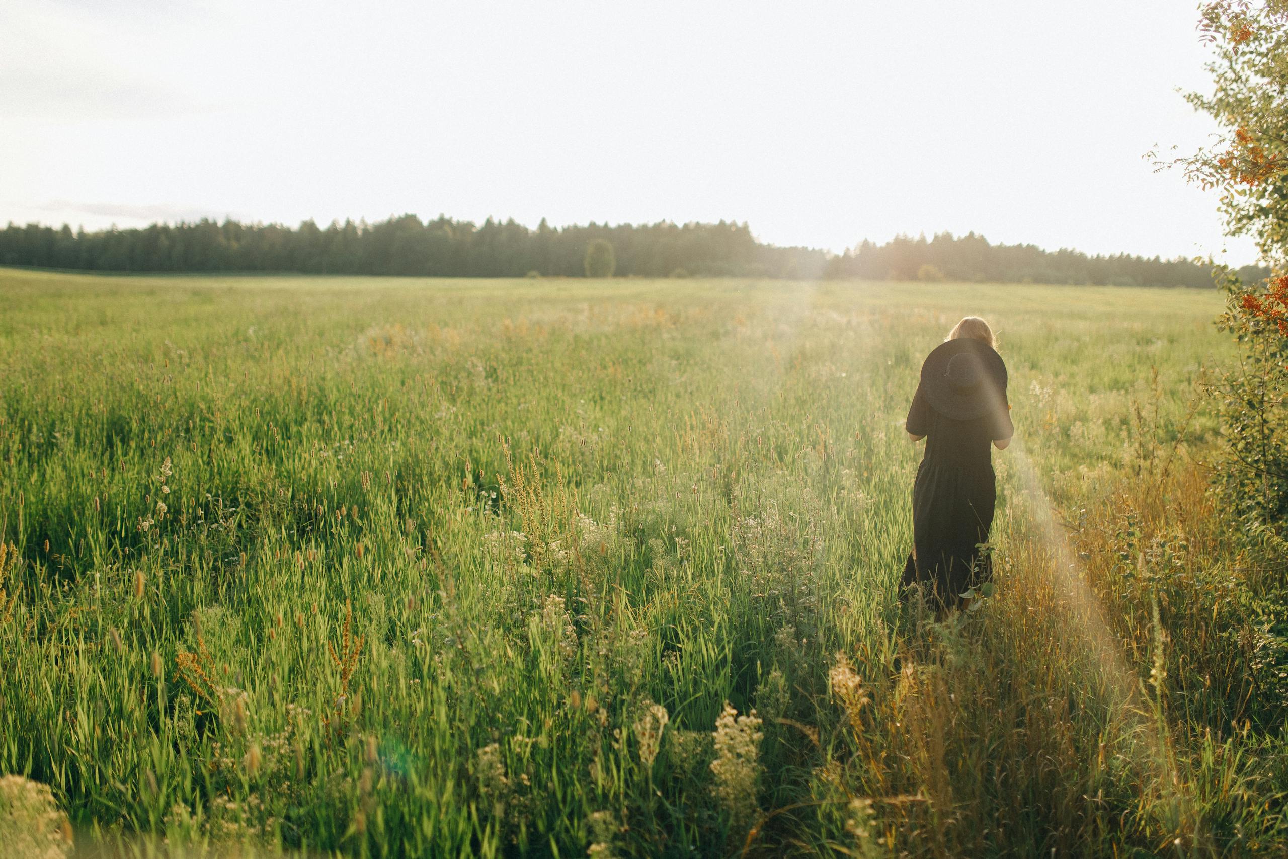 A serene scene of a woman walking through a lush, sunlit field during summer.